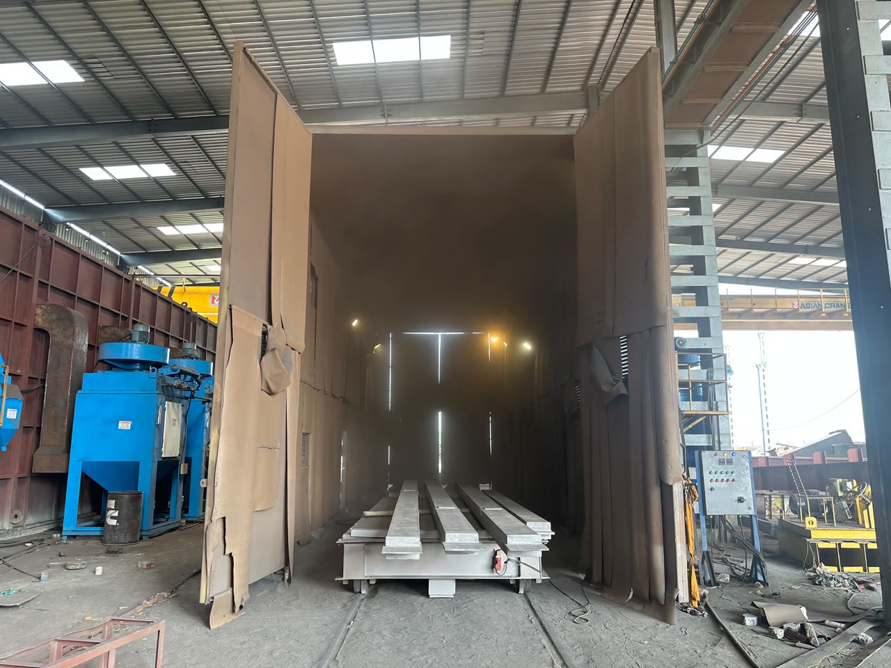Overhead EOT crane lifting a fabricated plate girder with a spreader beam in the fabrication shed
