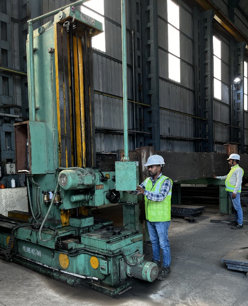 Overhead EOT crane lifting a fabricated plate girder with a spreader beam in the fabrication shed