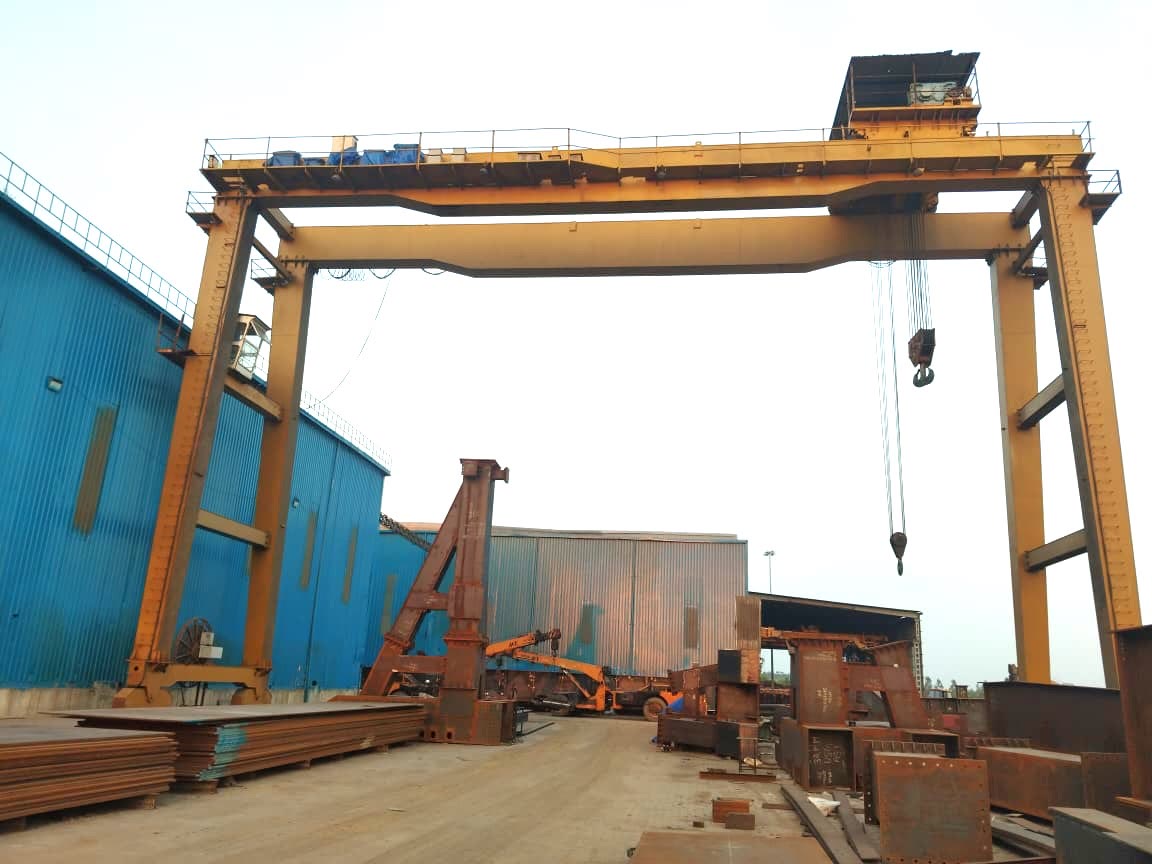 Overhead EOT crane lifting a fabricated plate girder with a spreader beam in the fabrication shed