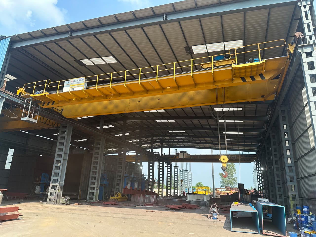 Overhead EOT crane lifting a fabricated plate girder with a spreader beam in the fabrication shed